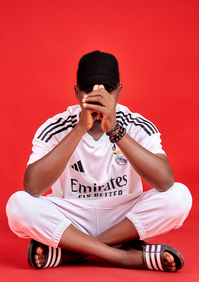 Man in white sportswear sitting on red background, showcasing casual style.